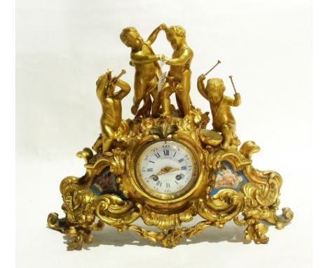 Late 19th century gilt metal mantel clock depicting putti playing instruments and dancing on rocky outcrop with rococo scroll