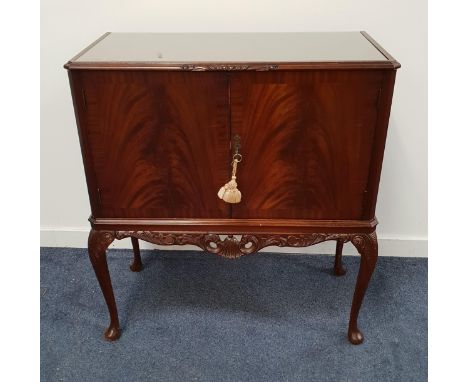 MAHOGANY DRINKS CABINETwith a pair of doors opening to reveal a mirrored back, shelf, drawer and two racks, with a carved fri