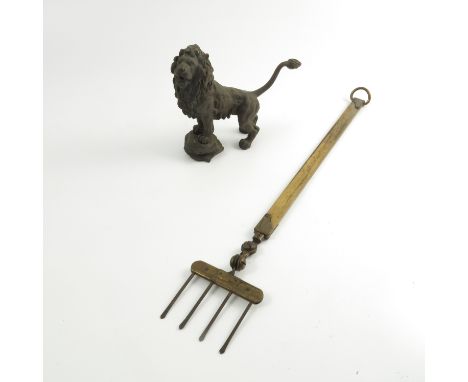 A metal model, of a lion with its front paws standing on a rock, height 6ins, together with a brass toasting fork with pivoti