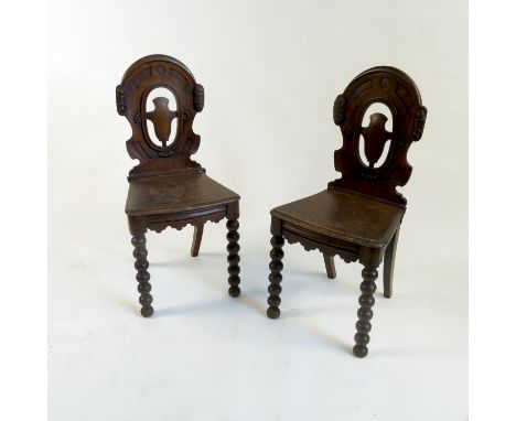 A pair of oak armorial hall chairs, raised on bobbin turned legs