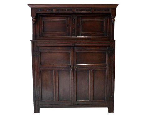 An Early 18th Century Oak Press Cupboard, the moulded cornice above a geometric carved frieze with inverted turned finials, t