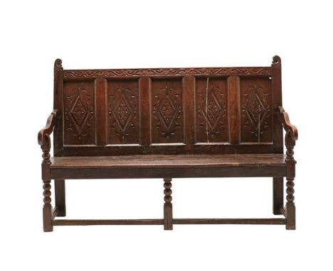 ^ An Early 18th Century Joined Oak Settle, the carved top rail above five lozenge carved panels and downswept arms, the seat 