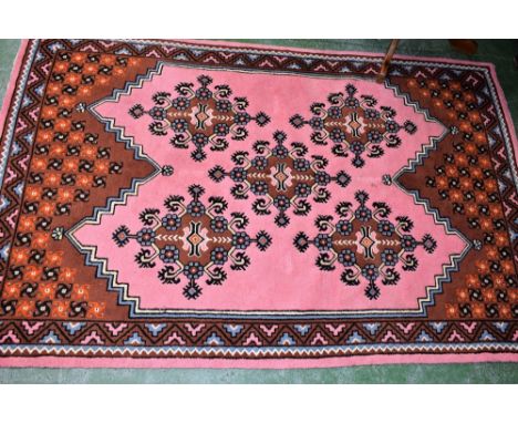 A Persian style carpet/rug, woven throughout with geometric motifs on a predominantly flamingo pink ground, 244cm x 158cm