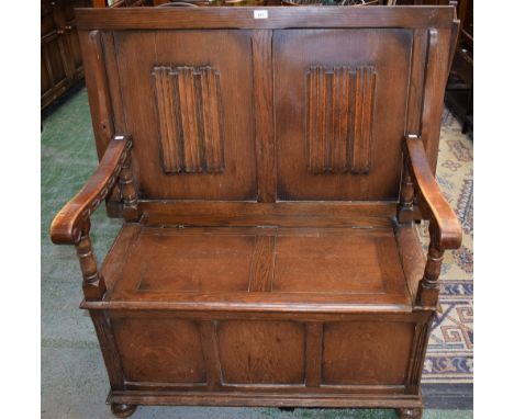 A Priory style monk's bench, rectangular top metamorphosing into the bench back, applied with linen folds, turned arm support