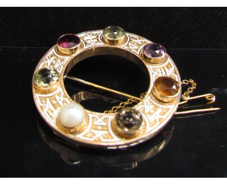 A circular gold brooch set with seven coloured stones and pearl with ornate white enamel and engraved design, 4.6cm diameter,