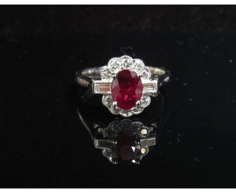 A white gold ruby and diamond ring the central oval ruby flanked by baguette cut diamond framed by round cut diamonds, stampe