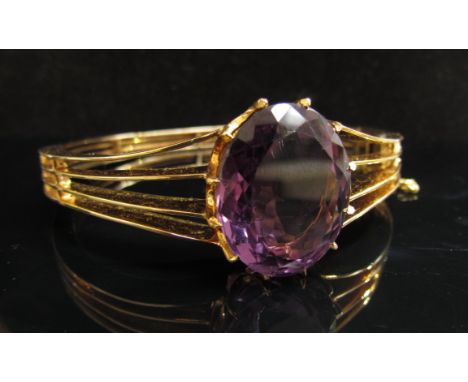 A gold bangle set with a large oval amethyst, 2.4cm x 1.8cm with open split claw design, unmarked, 33g