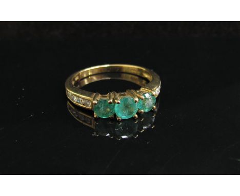 A 9ct gold emerald and diamond ring, three emeralds with diamond set shoulders. Size O, 2.5g