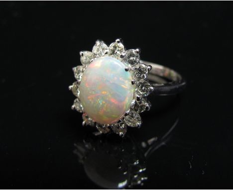 A white gold ring the central oval opal 10mm x 8mm framed by fourteen bright cut diamonds. Size K/L, 4.1g