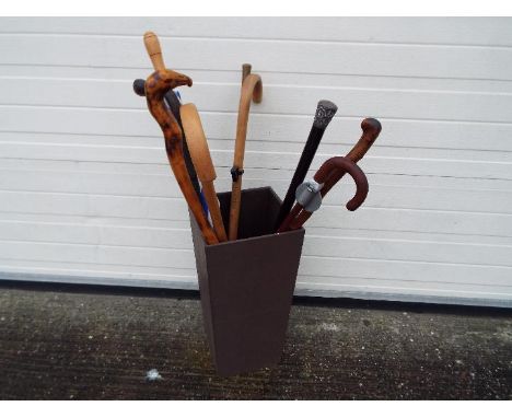 A stick stand containing a quantity of walking sticks including one with hallmarked silver mount, a shooting stick and simila