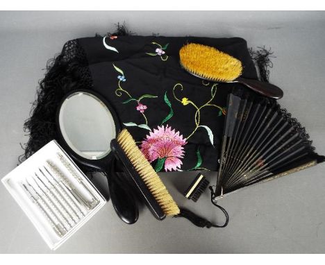 An ebony dressing table set comprising mirror and two brushes, a paper fan, embroidered scarf and a white metal nutcracker an