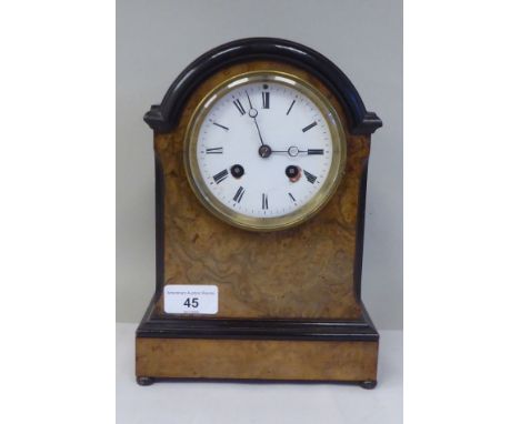 An early 20thC part lacquered walnut cased mantel clock with a round arch top and flank windows, on bun feet; the Camerer Kus