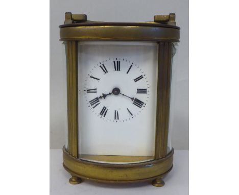 An early 20thC French oval brass cased carriage timepiece with bevelled glass panels and a folding top handle, on button feet