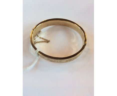 A 9ct. yellow gold bangle, hinged and of oval form, one half plain polished, the other engraved foliate scrolls, width 1mm, h
