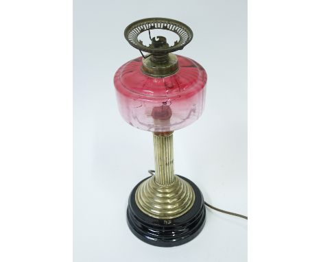 A brass column lamp, with a cranberry colour glass resevoir, on stepped black base