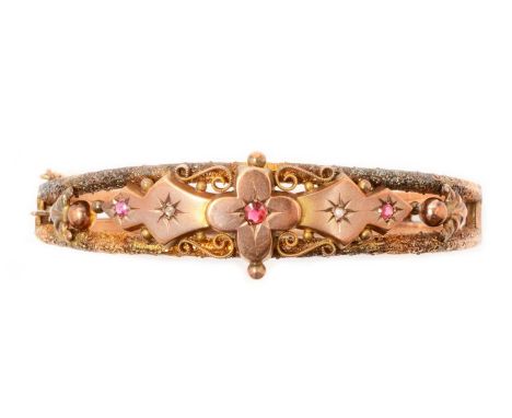 A 9ct yellow gold bangle, set with red stones, probably spinel, and rose-cut diamonds, in scrolling and textured floral mount