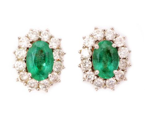 A pair of emerald and diamond cluster earrings, the oval facet cut emeralds measuring 5.8 x 4.1mm, surrounded by twelve brill