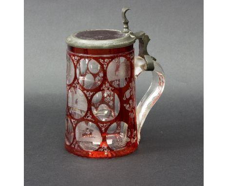 A Bohemian clear and ruby flash glass tankard, circa 1900, cut with lenses, some engraved with titled topographical scenes, 1