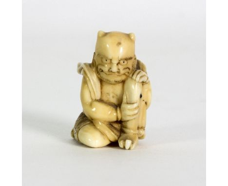 A Japanese carved walrus ivory figure of a squatting Oni, Meiji period, modelled applying moxa to an ulcer on his leg and a J