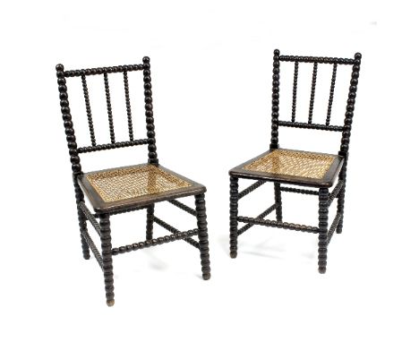 A pair of ebonised single chairs with cane seats and bobbin turned frames