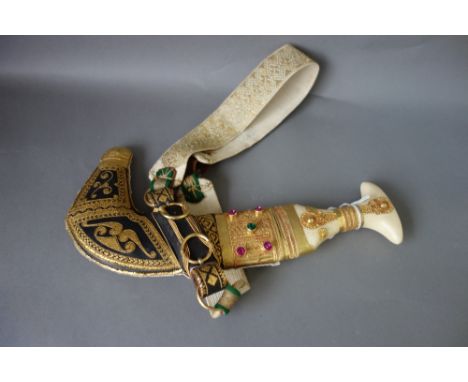 A late 20th century jambia, ornately decorated with gilt metal, housed in a leather scabbard.