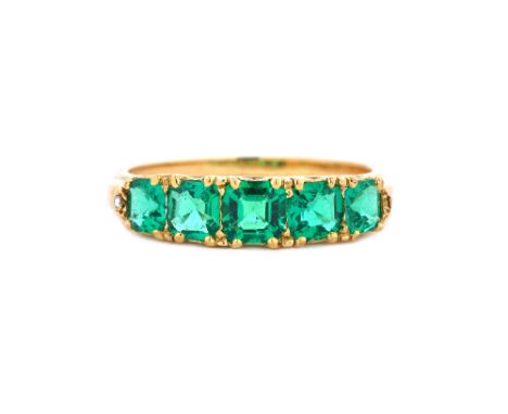 A gold and emerald set five stone ring, mounted with a row of graduated step cut emeralds, the mount decorated with pierced s