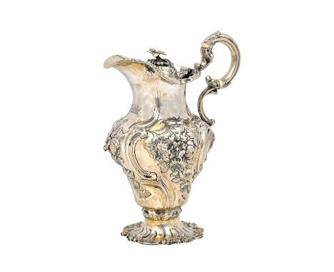 A Victorian silver hinge lidded small hot water jug, the body embossed with floral panels within scrolls, with an insulated s