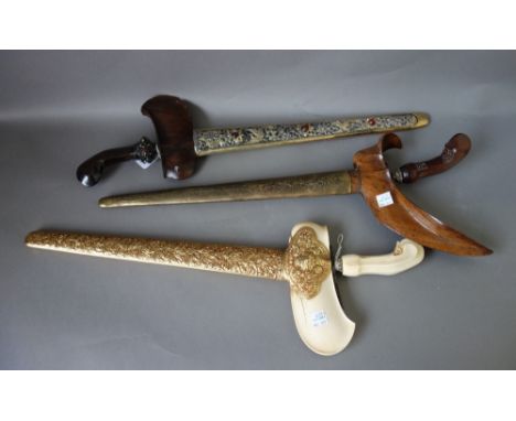 Three 20th century Sumatran kris, two with carved wooden handles, each with a metal bound wooden scabbard, (3).