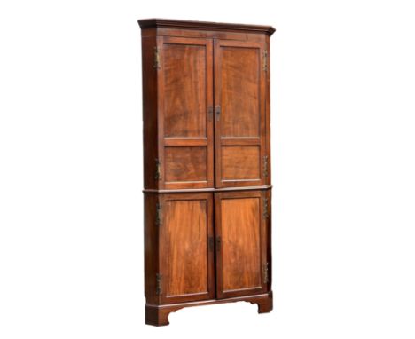A George II two piece floor standing red walnut corner cupboard the reel moulded cornice over a pair of two panel doors and a