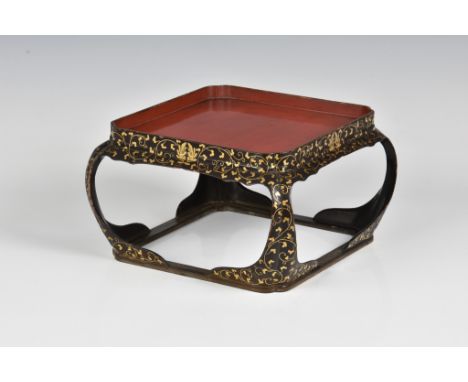 A Japanese lacquered wood square stand late 19th century, the red lacquer tray top on a black and gilt foliate decorated fram