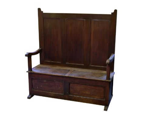 A George III panelled oak settle the eared, three panel back over a two panel hinged seat, swept arms on square chamfered sup