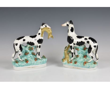 A pair of 19th century Staffordshire pottery coursing dogs with hares one having the hare in the mouth, one with hare lying b