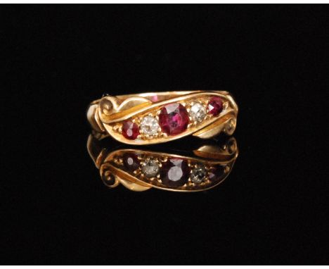 An 18ct hallmarked ruby and diamond scroll head ring, three graduated round cut rubies spaced by two old cut diamonds to scro