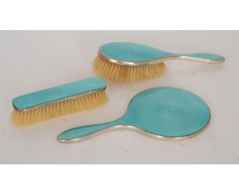 A hallmarked silver three piece brush set comprising two brushes and a mirror, each decorated with mint green guilloche ename