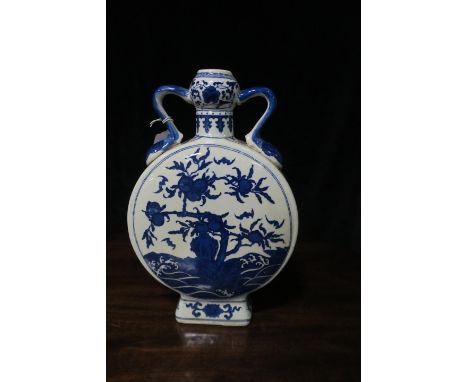 AN ORIENTAL GLAZED PORCELAIN MOON FLASK the white ground decorated with blue foliates with a pair of scrolled handles on rect