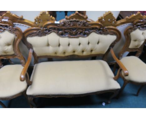 A CONTINENTAL STYLE MAHOGANY CARVED THREE PIECE SUITE comprising a two seater sofa with foliate pierced back, buttoned uphols