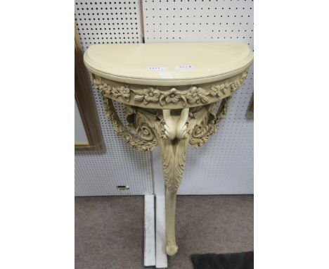 A WHITE PAINTED CONTINENTAL STYLE CONSOLE TABLE of demi-lune outline above the frieze decorated with foliates on a single cab