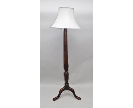 A STANDARD LAMP FORMED FROM A GEORGE III MAHOGANY BED POST, on fluted stem, the base carved with swags, on tripod supports wi