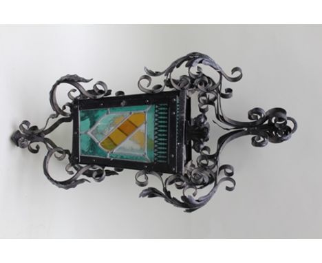 A WROUGHT IRON GOTHIC STYLE LANTERN with acanthus leaf and fleur-de-lys motifs, set with coloured leaded glass panels to the 