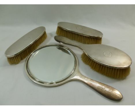 A George V silver backed four piece dressing table set comprised of three brushes and a hand mirror with engine turned decora