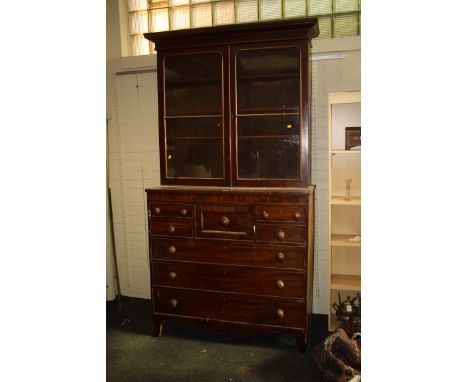 An early 19th century mahogany bookcase cabinet, the moulded cornice over a pair of glazed doors enclosing three shelves, the