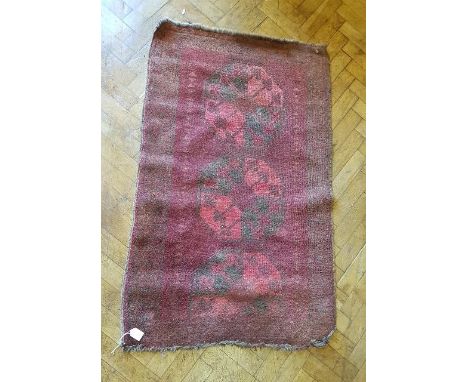 A vintage red ground Afghan mat with three elephant's foot guls, 134 x 82cm