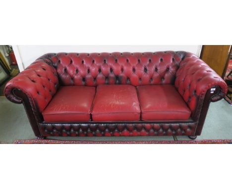 A 20th century oxblood leather upholstered button back chesterfield style three seater club sofa on bun feet, 74cm high x 197