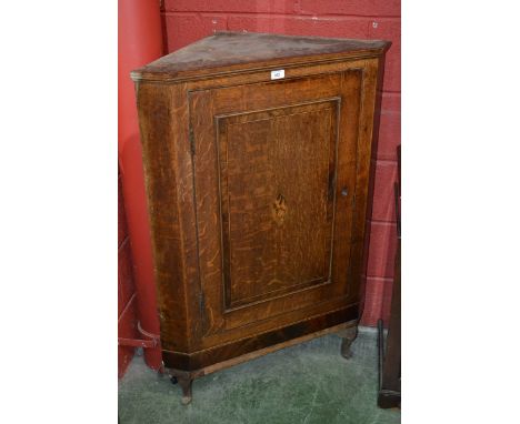 An oak corner cupboard, moulded cornice, crossbanded panel door, shell shaped cartouche, later cabriole supports.