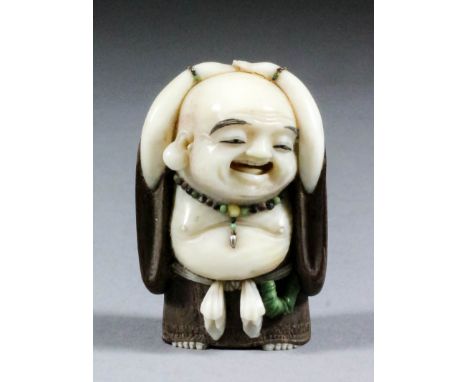 A Japanese carved ivory and wood netsuke of a standing Hotei, by Akishige, wearing a beaded necklace around his neck as he cl