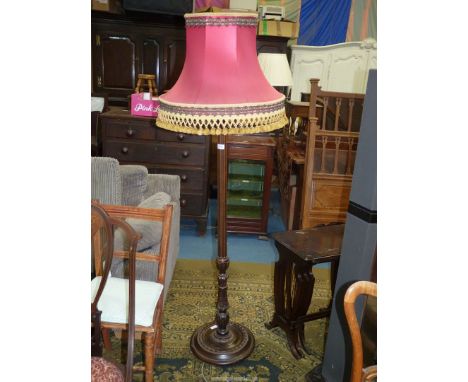 A standard lamp with a red shade having gold tassel edging.