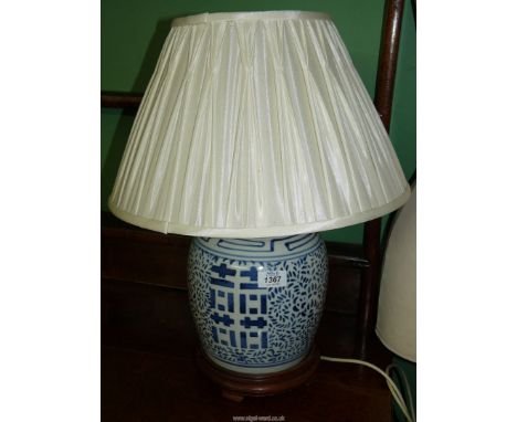 An Oriental blue and white ginger jar converted into a table lamp on wooden stand, with shade.