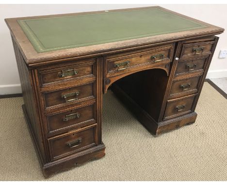 A late Victorian oak kneehole desk, the tooled and gilded leather insert top over a central drawer, flanked by two banks of f