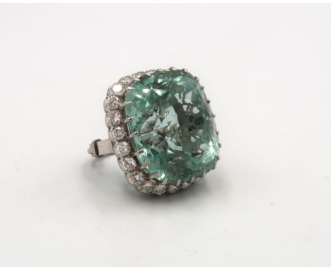 An aquamarine and diamond cluster ring. The cushion cut aquamarine estimated 74cts. Within a scalloped surround of 24 brillia
