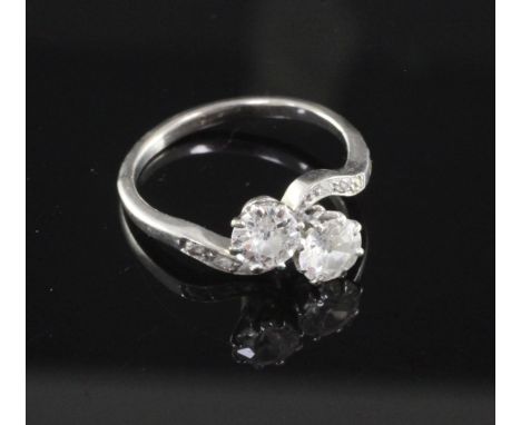 A platinum and two stone diamond crossover ring with diamond set shoulders, the tow round cut stones with an approximate tota